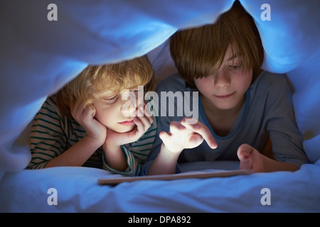 Brothers underneath duvet using digital tablet Stock Photo