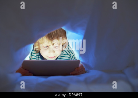 Boy underneath duvet using digital tablet Stock Photo