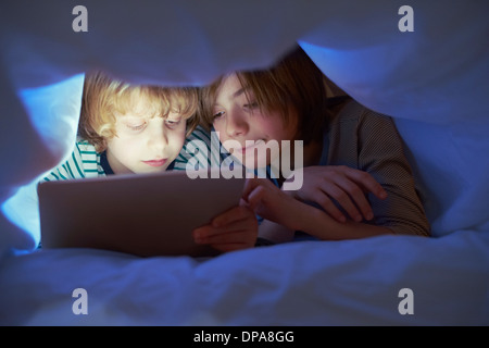 Brothers underneath duvet using digital tablet Stock Photo