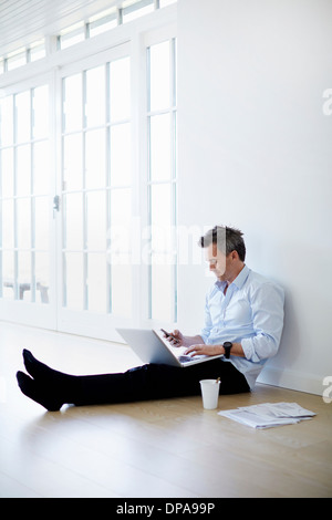 Man sitting on floor using laptop and phone Stock Photo