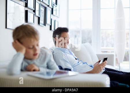 Father and son sitting on sofa using digital tablet and smartphone Stock Photo