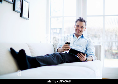 Man relaxing on sofa using digital tablet and smartphone Stock Photo