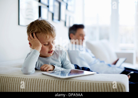 Father and son sitting on sofa using digital tablets Stock Photo