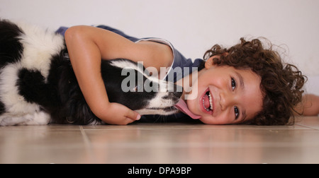 Young boy lying on floor hugging his pet dog Stock Photo