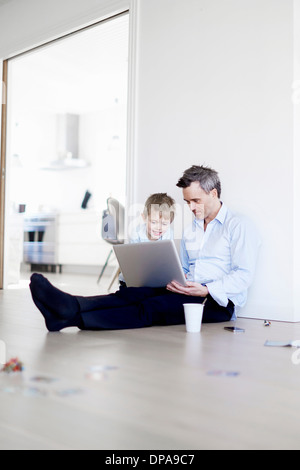 Man sitting on floor using laptop, son watching Stock Photo