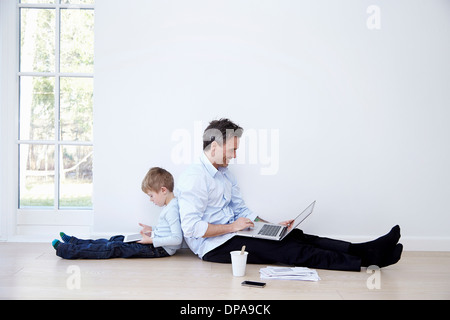 Father and son sitting back to back using laptop and digital tablet Stock Photo