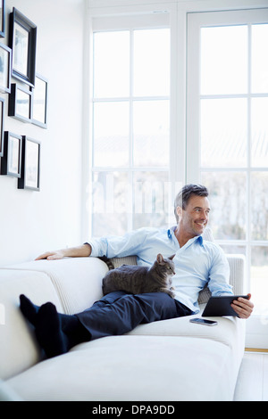 Man relaxing on sofa using digital tablet with cat Stock Photo