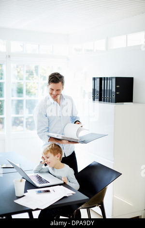 Boy using laptop and man looking at paperwork Stock Photo