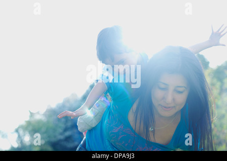 Boy riding on mother's back with arms stretched out Stock Photo
