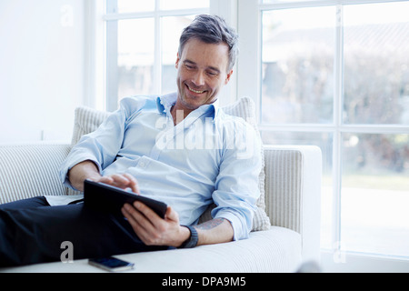 Man relaxing on sofa using digital tablet Stock Photo