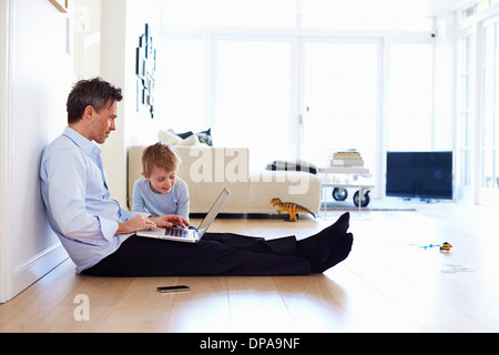 Man sitting on floor using laptop, son watching Stock Photo