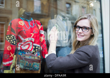 Woman cleaning window of clothes shop Stock Photo