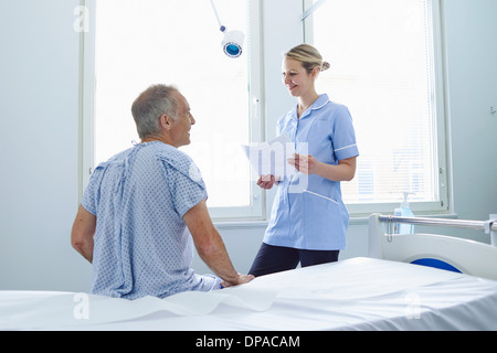 Nurse standing talking to patient sitting on hospital bed Stock Photo