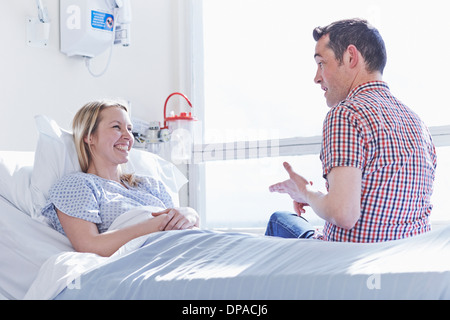 Patient lying in hospital bed talking to visitor Stock Photo