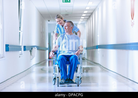 Nurse pushing patient in wheelchair down corridor Stock Photo