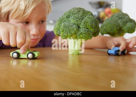 Boy playing cars around broccoli trees Stock Photo