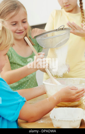 Children baking, sieving flour into mixing bowl Stock Photo