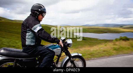 Senior male riding motorbike through rural landscape Stock Photo