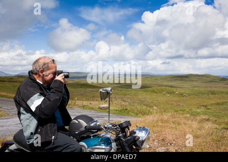 Senior male motorcyclist taking a photograph of scene Stock Photo