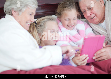Grandparents and grandchildren playing digital game in bed Stock Photo