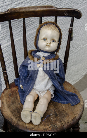 Vintage child's doll sitting on an old chair outside a junk shop in Edinburgh, Scotland, UK. Stock Photo