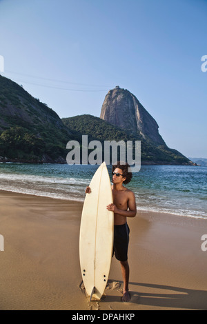 Man holding surfboard on beach, Rio de Janeiro, Brazil Stock Photo