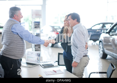 Car salesman and couple shaking hands in car showroom