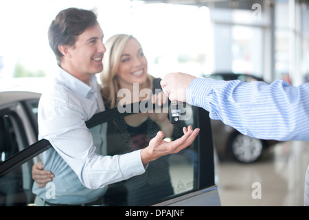 Car salesman handing key to couple in showroom Stock Photo