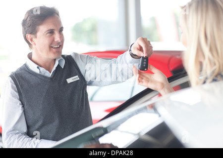 Car salesman handing keys to young woman in showroom Stock Photo