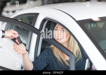 Young woman sitting in new car with key in showroom Stock Photo