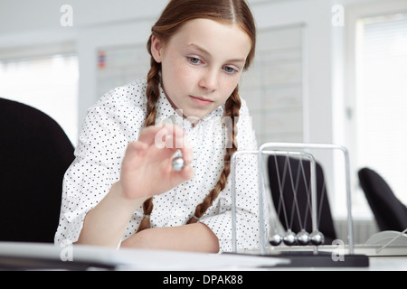 Girl playing with newton's cradle on desk Stock Photo