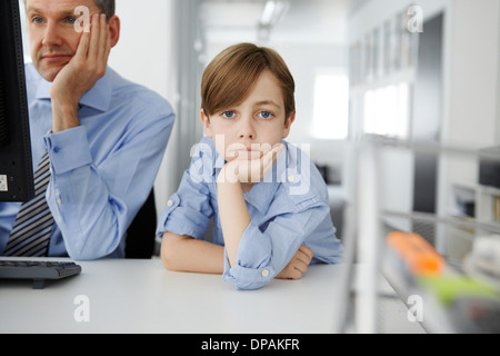 Boy leaning on elbow, father using computer Stock Photo