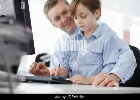 Boy sitting on father's lap using computer keyboard Stock Photo
