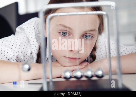 Girl playing with newton's cradle on desk Stock Photo