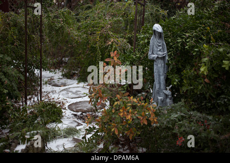 A stone sculpture of St. Francis of Assisi decorates a garden near a stone path covered with snow in Lancaster, TX, USA Stock Photo