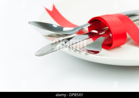 Fork, spoon and knife tied up with red ribbon on a plate Stock Photo