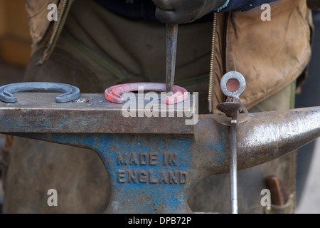 Farrier hammering red hot glowing horseshoe on anvil. Stock Photo