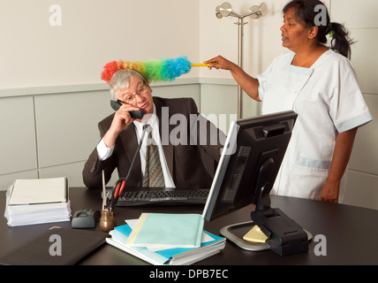 Funny cleaning woman cleaning the office of the manager including his face Stock Photo