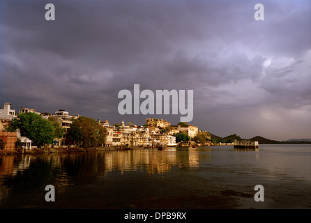 A view across Lake Pichola to the bathing ghats and the City Palace in Udaipur in Rajasthan in India in South Asia. Sunset Sky Storm Weather Monsoon Stock Photo