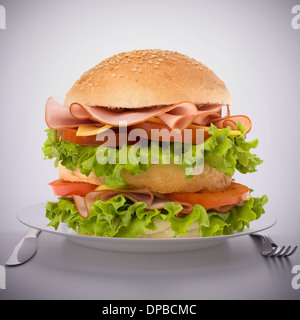 Fast food big sandwich with lettuce, tomato, smoked ham and cheese on plate Stock Photo