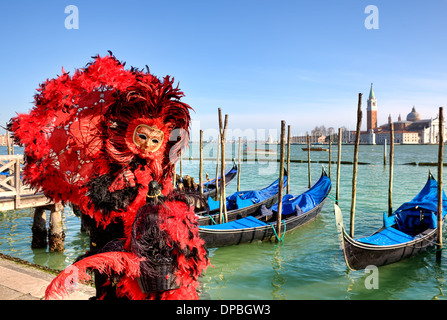 Participant wear red costume and mask standing near gondolas on Grand Canal during carnival in Venice, Italy. Stock Photo