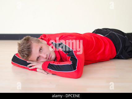 Attractive young man laying on the floor wearing gym suit or tracksuit, looking at camera Stock Photo