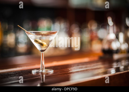 One glass of famous Classic Cocktail Dry Martini with Olive, shot on location on wooden Bar. Stock Photo
