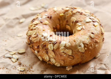 Multi-grain bagel covered in oats and seeds on crinkled brown paper Stock Photo