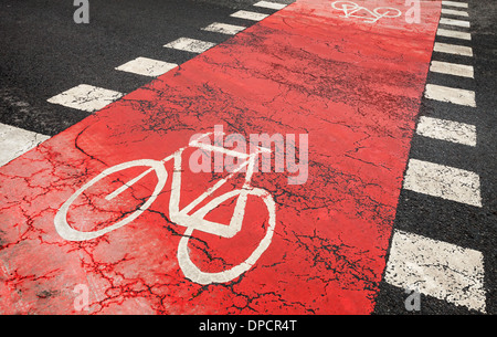 Red bicycle road marking on urban asphalt road crossing Stock Photo