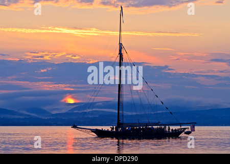 The sun setting behind the Sloop Clearwater on the Hudson River out for a sunset cruise Stock Photo