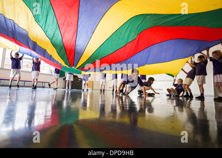 Pupils at a UK primary school playing with a parachute in the school hall Stock Photo