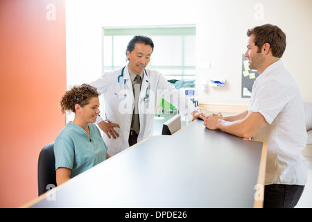 Medical Team Working On Computer While Man Standing At Reception Stock Photo