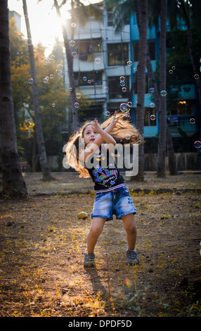 A little girl is trying to catch soap bubbles on a warm summer evening in a park. Stock Photo