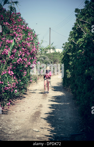 walking girl with straw hat between some blooming bushes in summer. Stock Photo